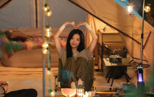景甜坐在帐篷旁对着镜头比心,十分甜美迷人。