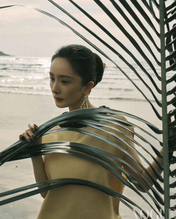 杨幂手持棕榈叶轻遮身侧,暖调造型衬得气色柔和。