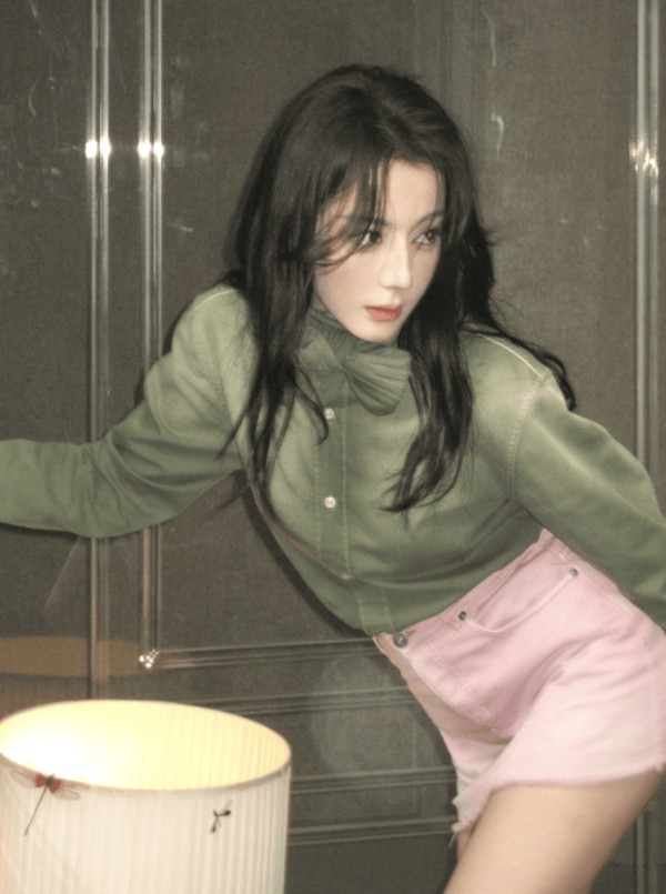 迪丽热巴穿绿调上衣搭配粉色短裙，姿态随性舒展。