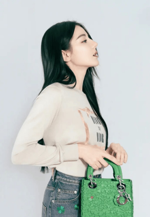 迪丽热巴侧身抬眸，绿色手袋点缀造型慵懒松弛。