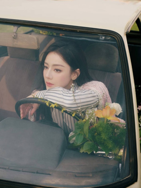 迪丽热巴手搭方向盘，身旁鲜花环绕，眼神温柔，治愈浪漫。