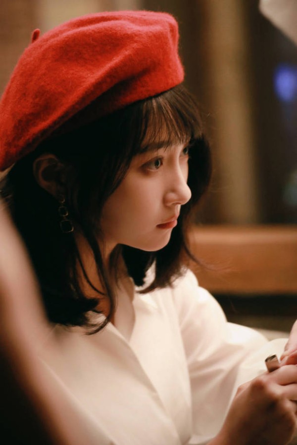 关晓彤头戴红色贝雷帽,身着白衬衫,侧眸凝视,在暖光中尽显温柔文艺的气质。